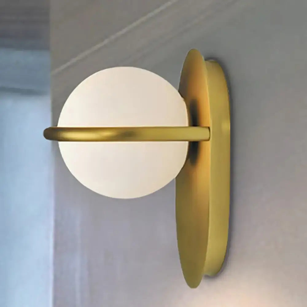 Gold-toned wall light with frosted milk glass globe and black metal backplate featuring minimalist circular design