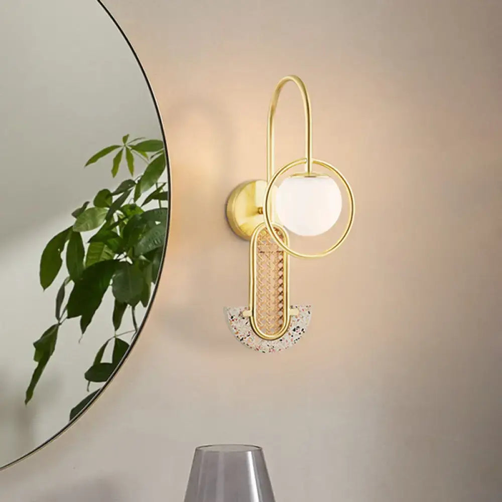 Modern black and gold wall sconce with a gold-toned arm, opal glass ball, and woven rattan accent for bedroom lighting