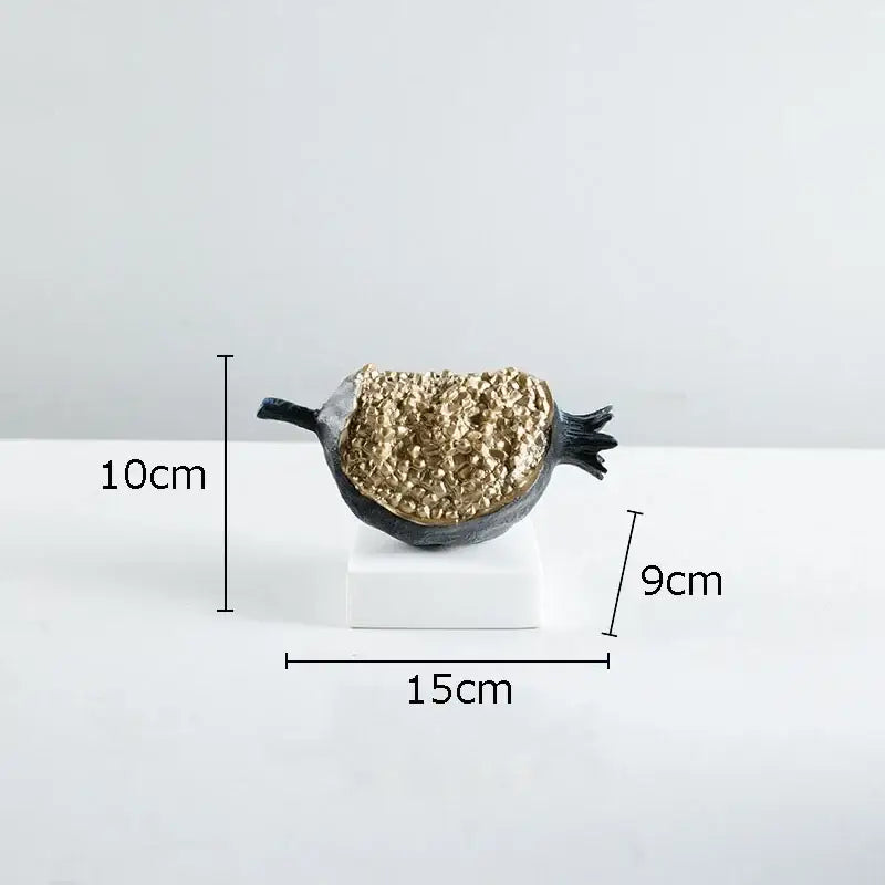 A sleek black and gold resin decorbites golden pomegranate sculpture with a textured crystalline interior on a white base