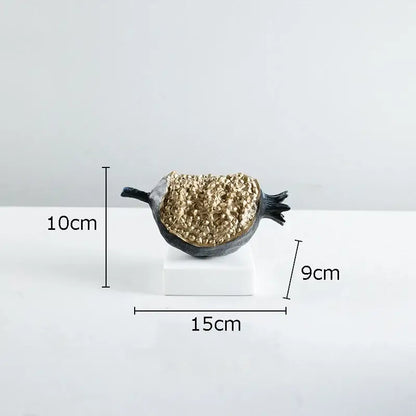 A sleek black and gold resin decorbites golden pomegranate sculpture with a textured crystalline interior on a white base