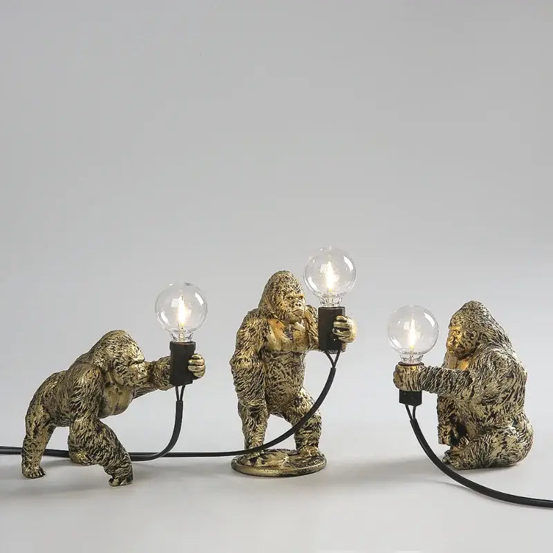 Three golden resin gorilla night light figurines holding lit bulbs connected by black cords decorbites gorilla night lamp