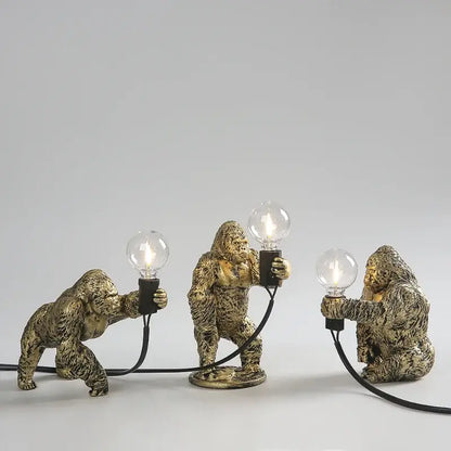 Three golden resin gorilla night light figurines holding lit bulbs connected by black cords decorbites gorilla night lamp