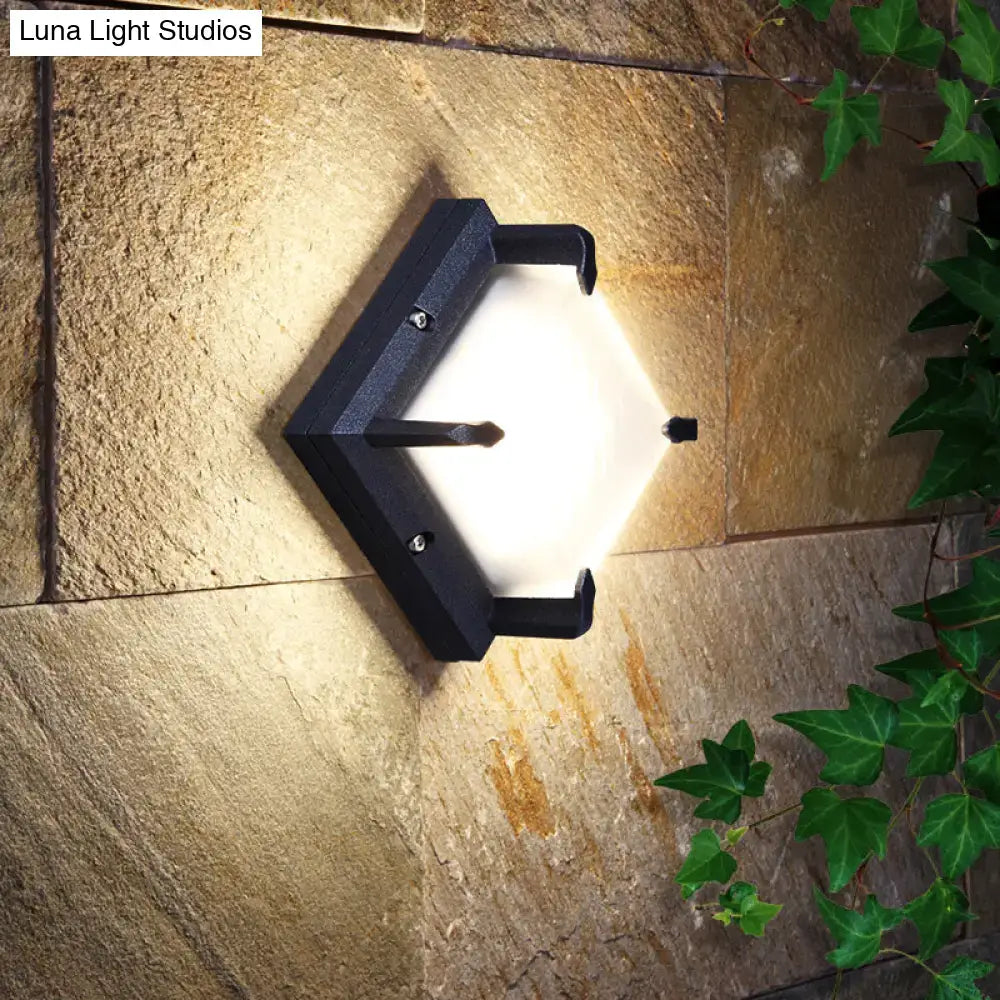 Modern black hexagonal metal square patio wall sconce with frosted glass panel emitting warm light