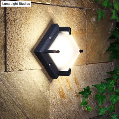Modern black hexagonal metal square patio wall sconce with frosted glass panel emitting warm light