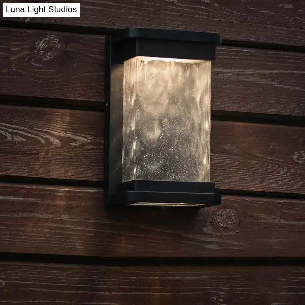 Modern black led outdoor wall sconce with rippled glass cylinder diffusing warm light through textured translucent panel