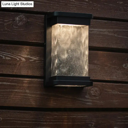 Modern black led outdoor wall sconce with rippled glass cylinder diffusing warm light through textured translucent panel