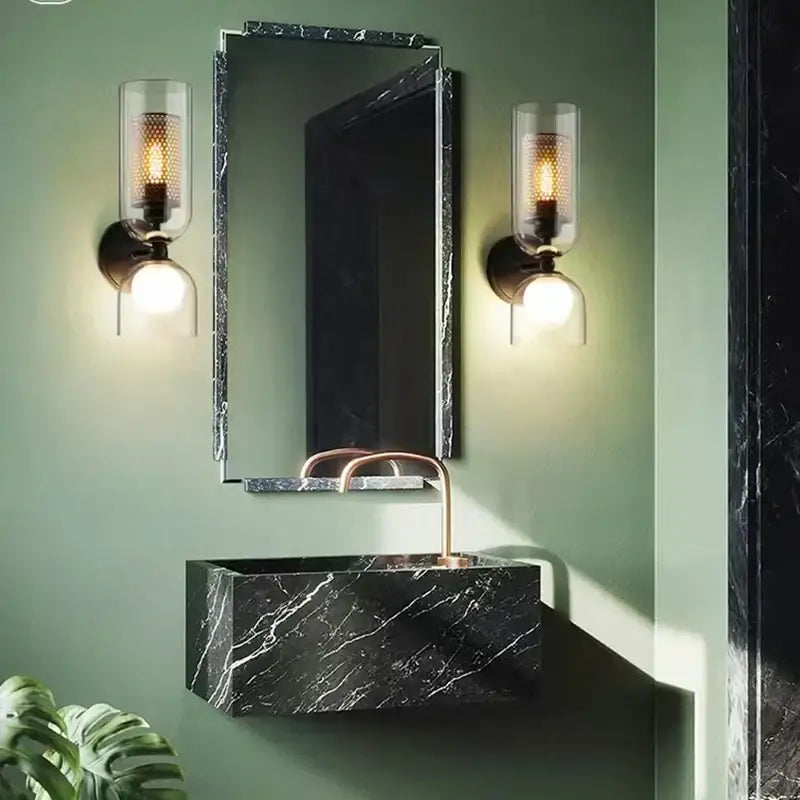 Modern black metal wall light with clear glass shade shown above black marble rectangular sink with polished copper faucet