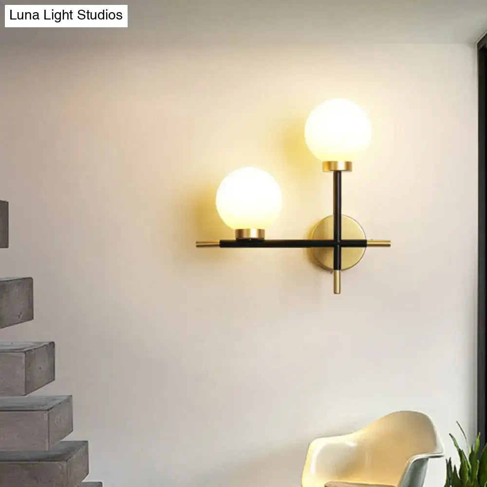 Modern black wall mount light fixture with two milk glass frosted globes and gold toned hardware for foyer use