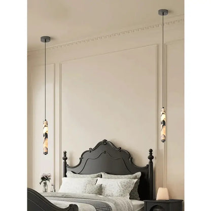 Two modern black pendant lights with natural marble stone cylindrical shades hang above a dark wooden bed frame