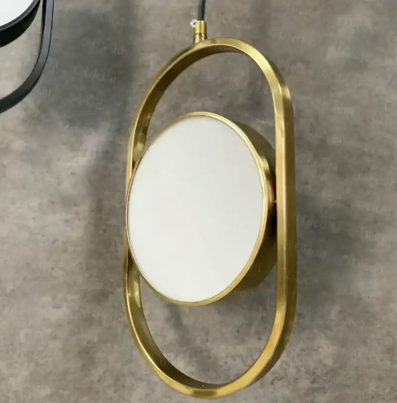 Gold-framed oval mirror paired with modern black pendant light featuring adjustable angle for dining room decorbites design