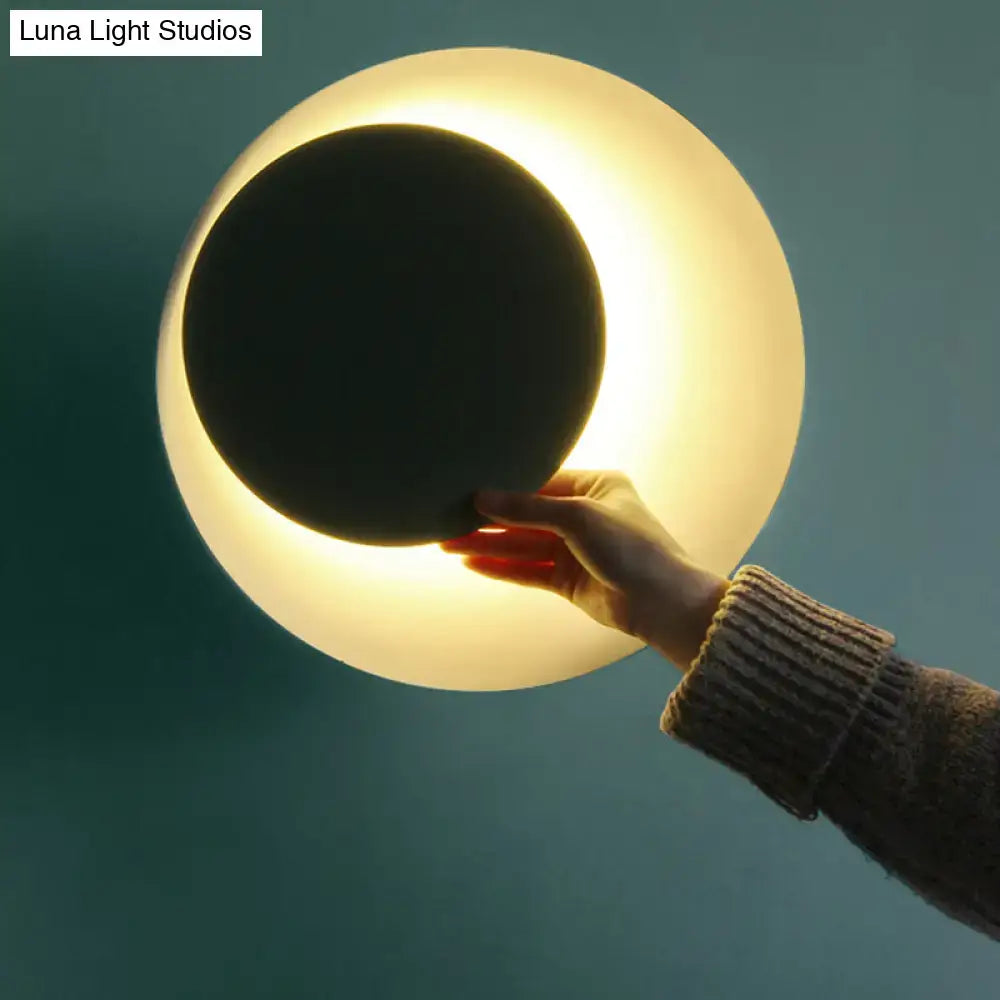 Modern black and pink circle sconce light fixture with soft glowing spherical lamp and black circular cutout for bedroom use