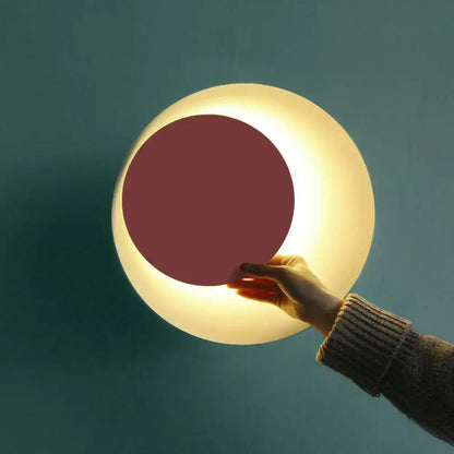 Modern black and pink circle sconce light fixture with a matte white shell and warm glowing maroon inner circle for bedroom use