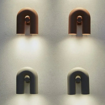 Two minimalist u-shaped tube wall lamps in terracotta and matte gray ceramic with central circular accents for bedrooms