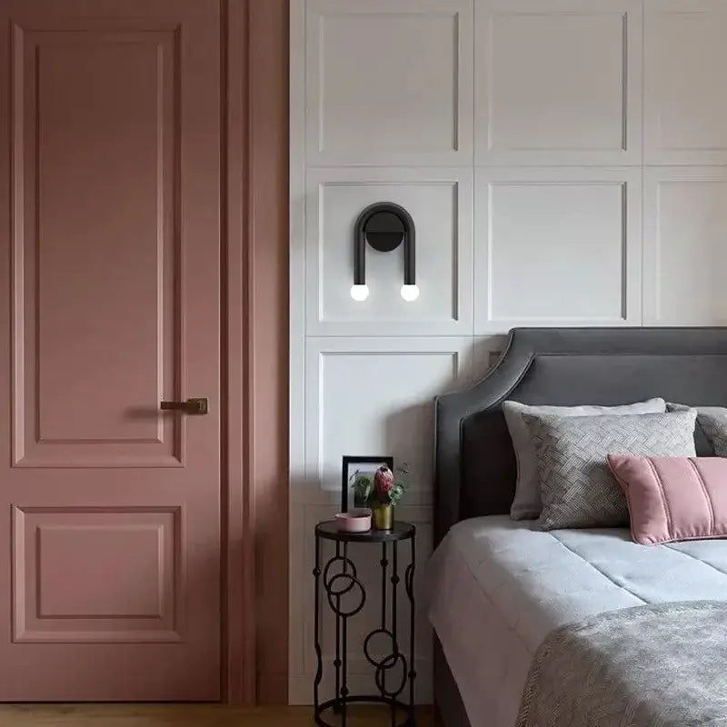 Modern black u-shape led wall lamp with spherical bulbs mounted above gray upholstered bed with pink patterned pillows