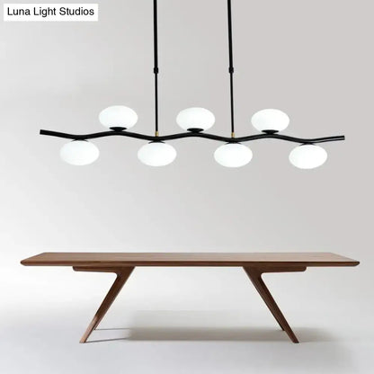 Modern black wavy pendant light with five white glass globes suspended above a wooden dining table by DecorBites