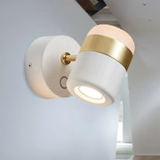 Modern black and white rotatable led spotlight wall sconce with matte white ceramic body and polished gold band lighting a bedroom