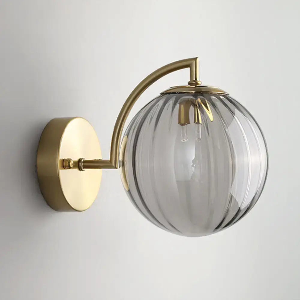 A sleek modern wall sconce with a gold finish and ribbed smoked glass globe for bedroom lighting