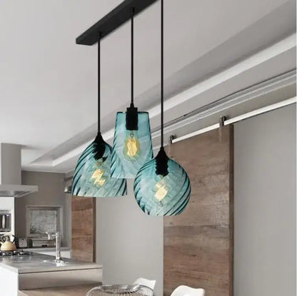 Three teal glass led pendant lamps with textured ribbed design hang from black cords for dining room lighting