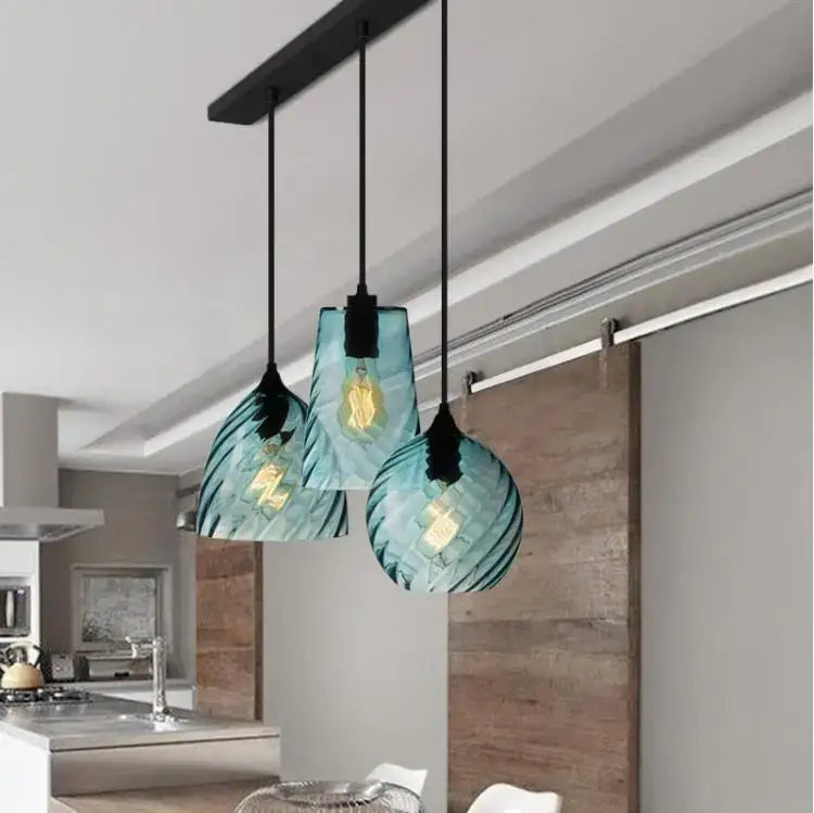 Three teal glass led pendant lamps with textured ribbed design hang from black cords for dining room lighting