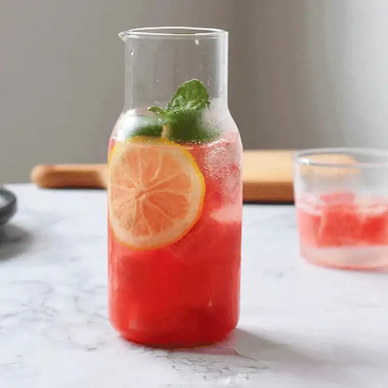 A modern borosilicate glass drinkware set featuring a clear carafe filled with red iced beverage and orange garnish