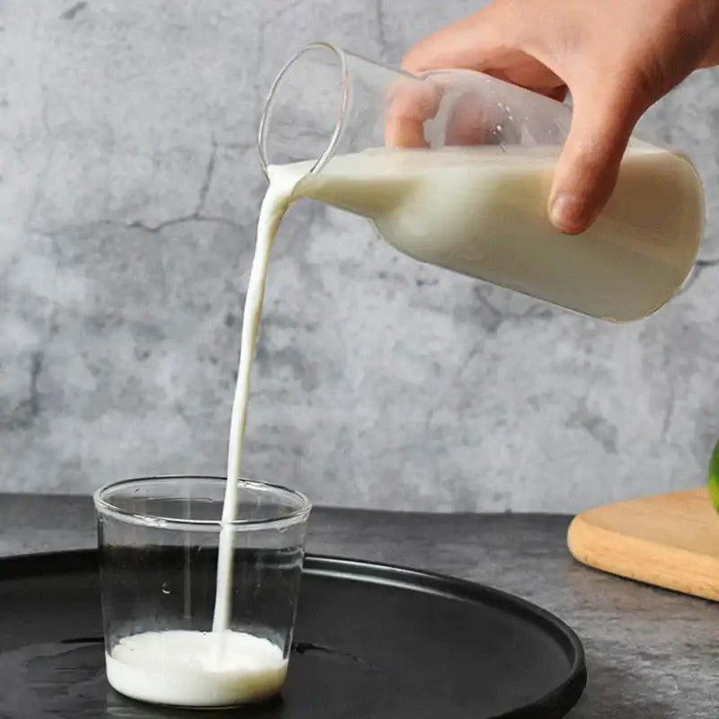 A modern borosilicate glass drinkware set features a clear glass pitcher pouring milk into a matching transparent tumbler