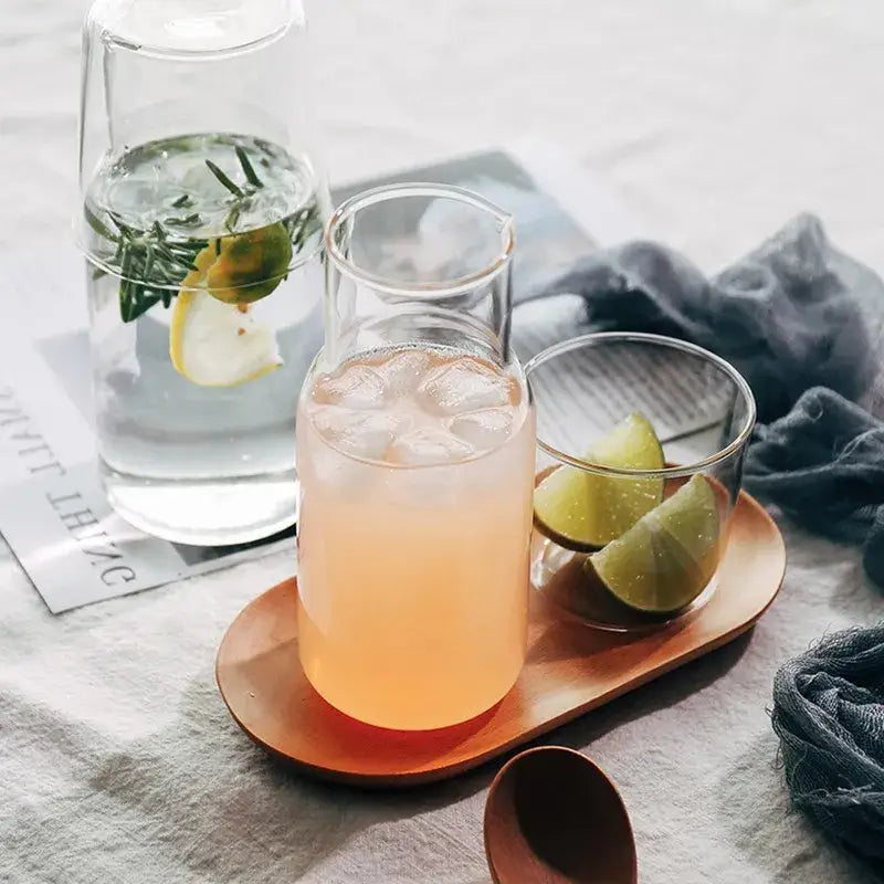 A modern borosilicate glass drinkware set with a clear glass pitcher filled with iced pinkish-orange beverage and lime slices