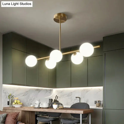 Modern brass pendant light with five spherical glass shades arranged along a horizontal bar for dining room use