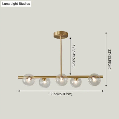 Modern brass 5-light pendant light with spherical glass shade and clear globes arranged horizontally for dining room