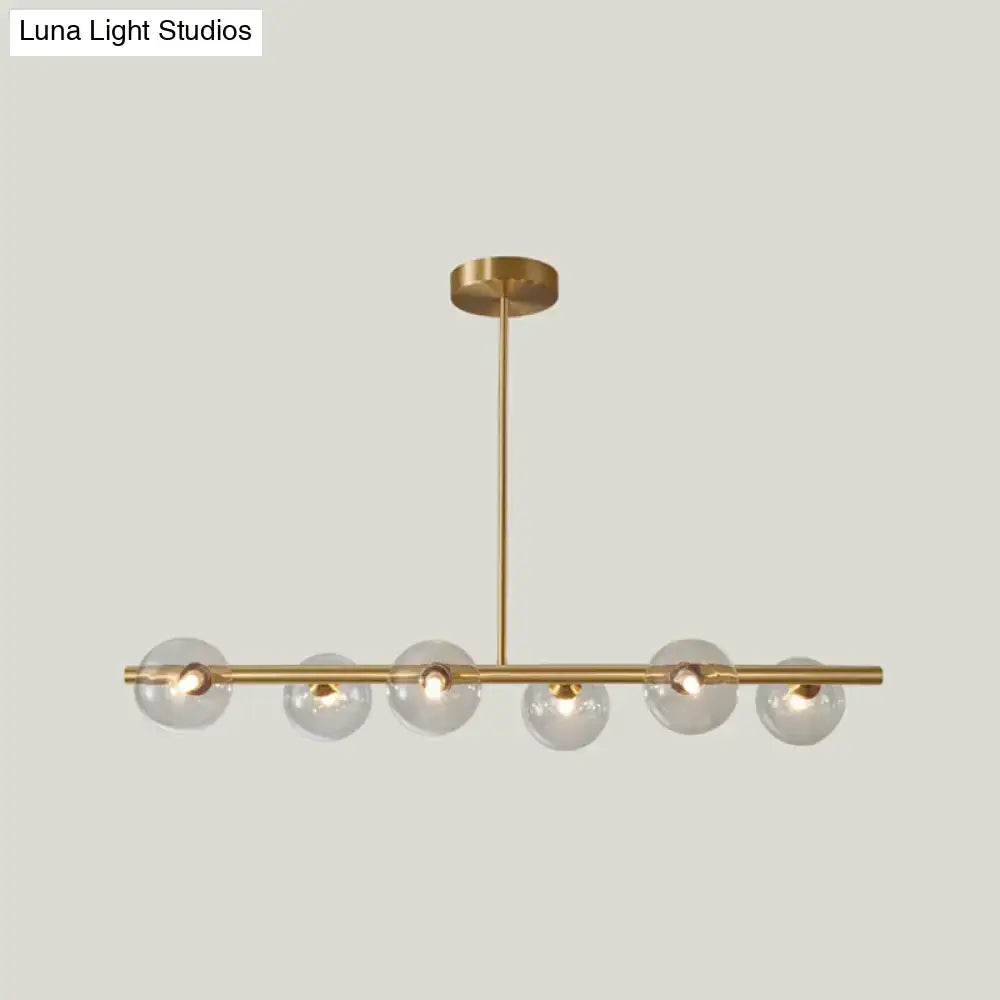 Modern brass pendant light with six gold-toned spherical glass shades on a horizontal bar for dining room lighting