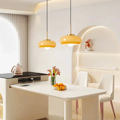 Two modern brass and amber glass pendant lights with copper bauhaus led fixtures hang above a white dining table