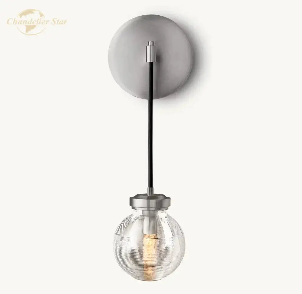 Modern brass and black crystal led wall sconce with matte gray backplate, black stem, and clear textured glass globe