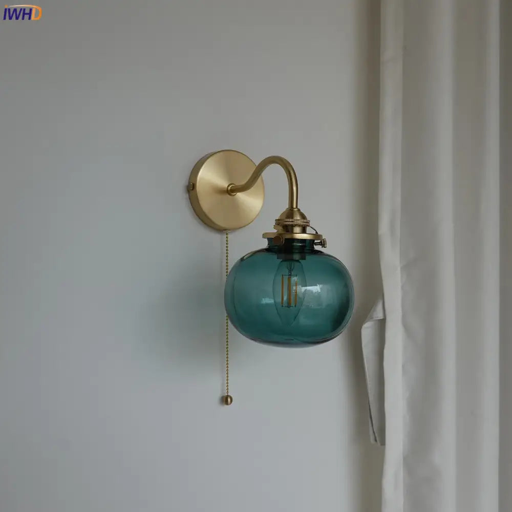 Modern brass wall sconce with a teal blue glass ball shade and exposed filament bulb with pull chain switch