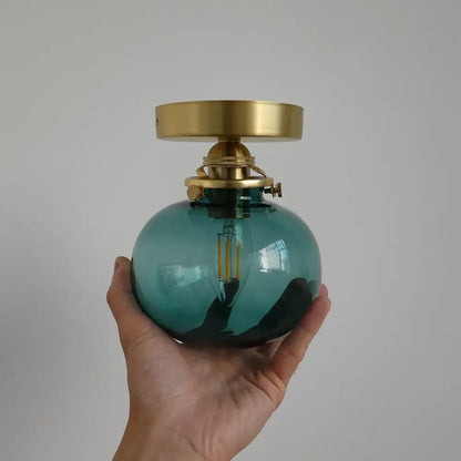 Modern brass and blue glass ball wall sconce with teal glass ball and brass fittings for bedroom lighting