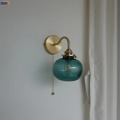 Modern brass and blue glass ball wall sconce featuring a teal glass ball with exposed filament bulb and pull chain switch