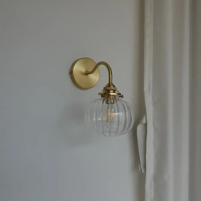 Modern brass wall sconce with a blue glass ball and clear ribbed globe housing an exposed filament bulb for bedroom use