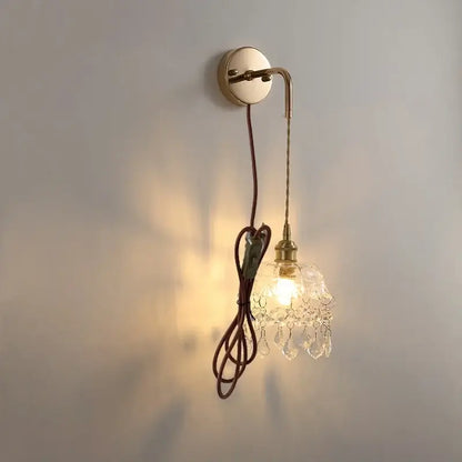 Modern brass wall lamp featuring clear glass crystal chandelier shade and braided brown cord for elegant bedroom lighting decorbites clear glass