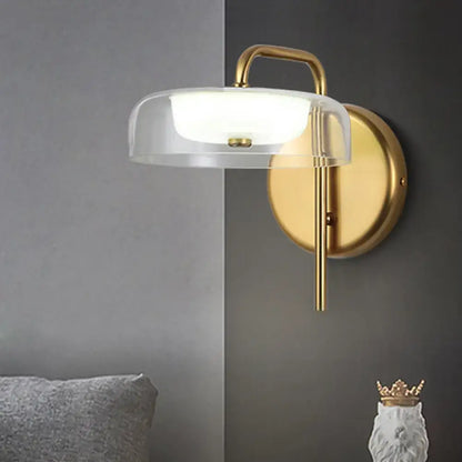 Modern brass and glass bedside wall sconce with clear glass dome and frosted white light diffuser for bedroom lighting