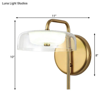Modern brass and glass bedside wall sconce with a clear glass dome and elegant curved arm for bedroom lighting