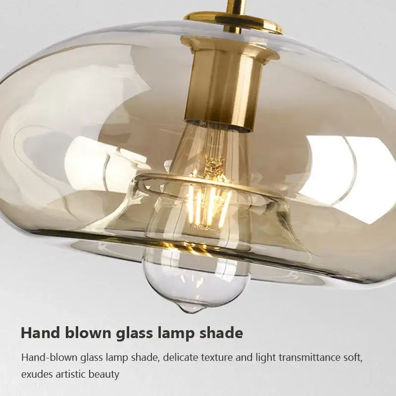 Modern brass and glass pendant light with amber lamp shade, gold metal accents, iron finish, and cord pendant installation
