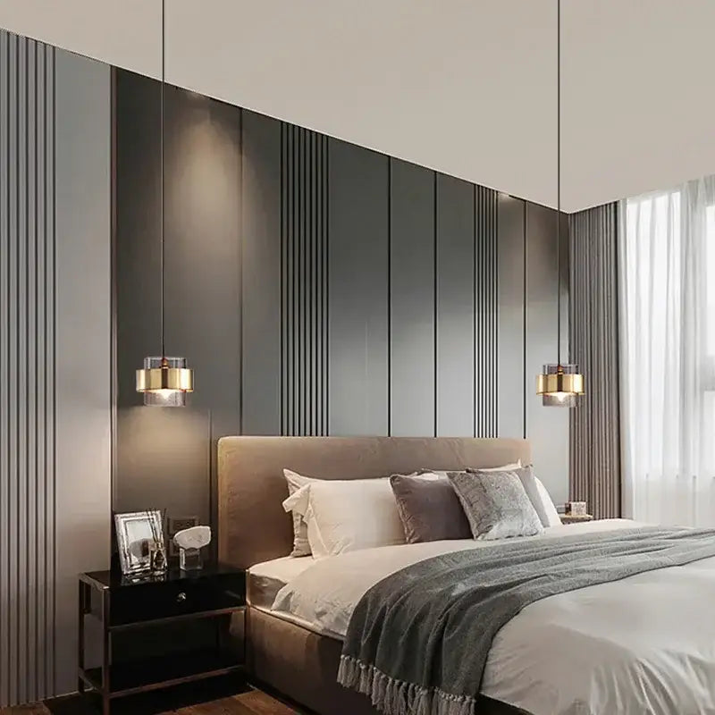 Modern brass and glass pendant light above a modern bed with beige upholstered headboard and layered pillows