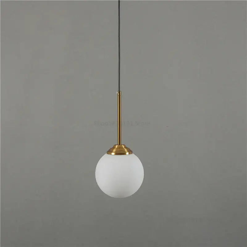 Modern brass and glass pendant lights featuring a frosted white glass globe suspended by a slender brass stem for kitchen dining room