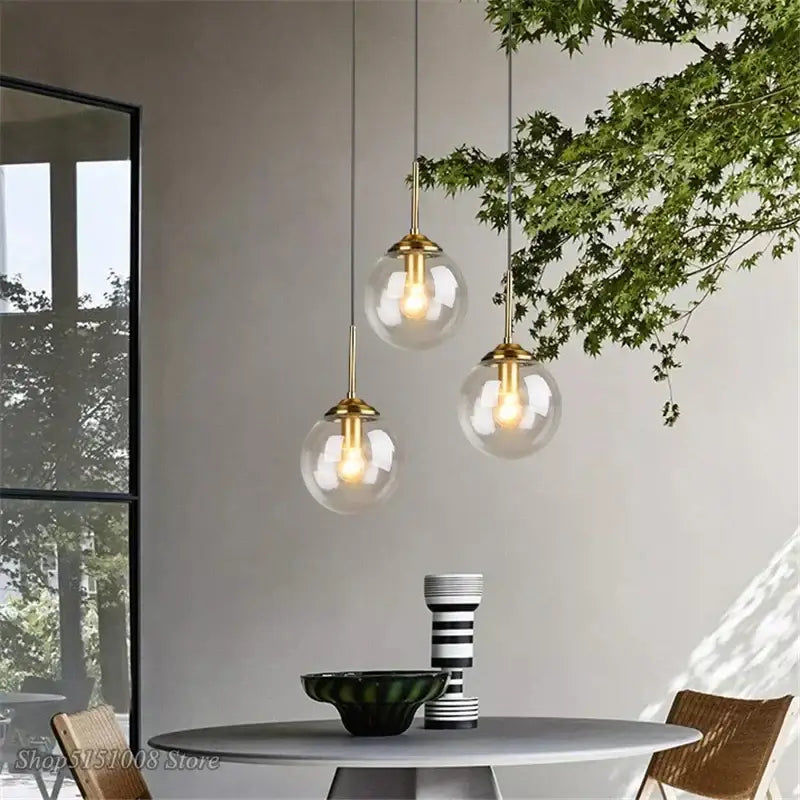 Three elegant modern brass and glass pendant lights with glass globes hang from the ceiling for kitchen or dining room