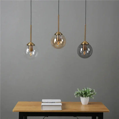 Three modern brass and glass pendant lights with clear amber and dark gray glass shades above wooden table