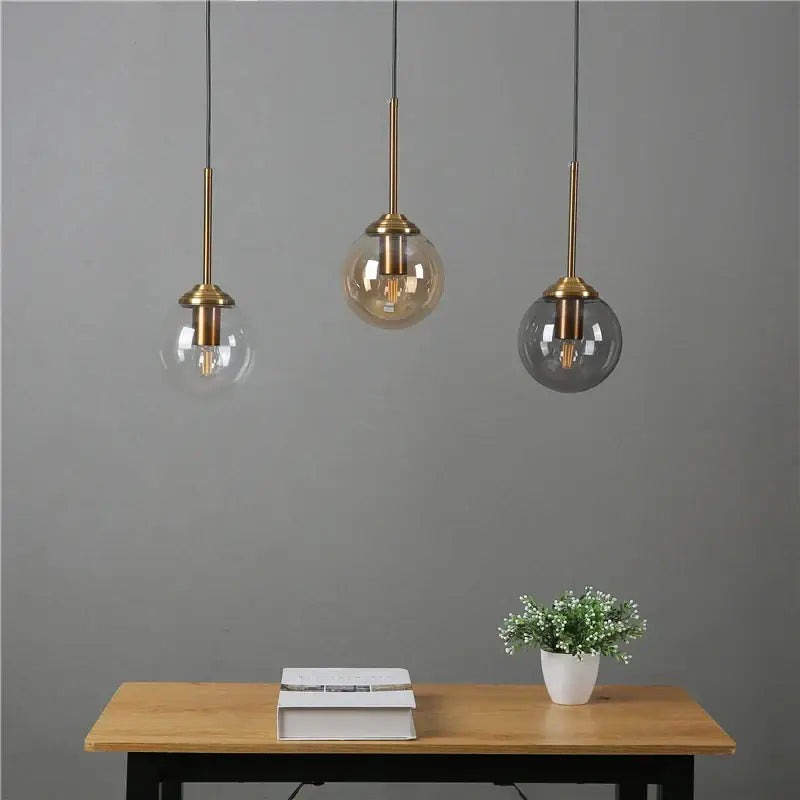 Three modern brass and glass pendant lights with clear amber and dark gray glass shades above wooden table