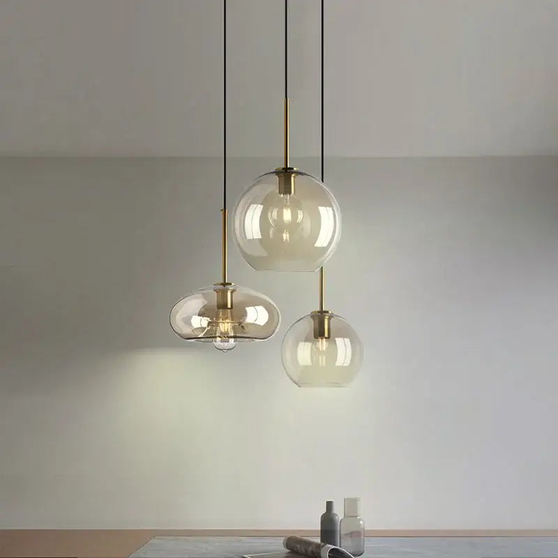 Three modern pendant lights with clear glass globes and brass accents hang from black cords for kitchen or dining room