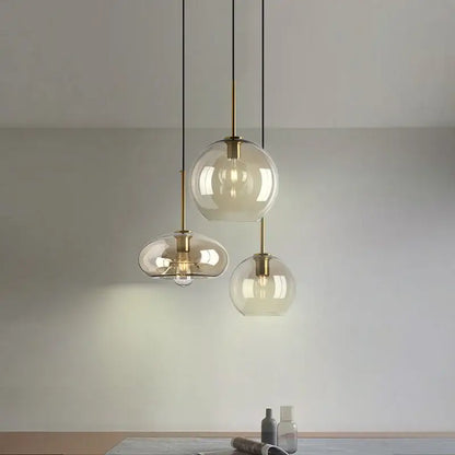 Three modern pendant lights with clear glass globes and brass accents hang from black cords for kitchen or dining room