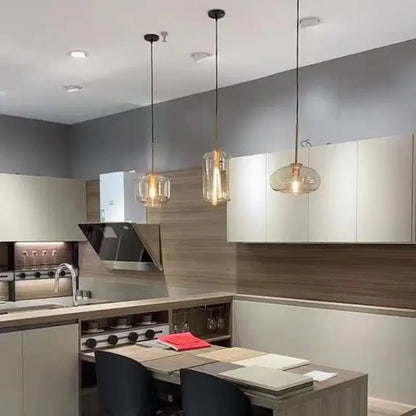 Three modern brass and glass pendant lights with glass shades hang above a kitchen island for dining room lighting