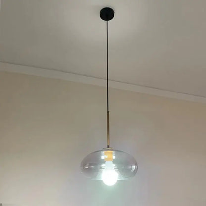 Modern brass and glass pendant lights featuring a clear glass dome, brass rod, and black cord for kitchen or dining room