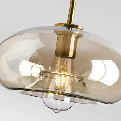 Modern brass and glass pendant light with translucent amber shade and exposed filament bulb for kitchen and dining room