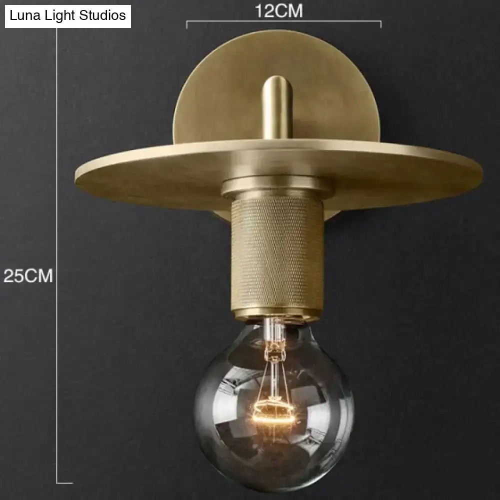 Modern brass and glass wall sconce featuring a brass finish, circular backplate, textured stem, and exposed bulb for bedroom lighting